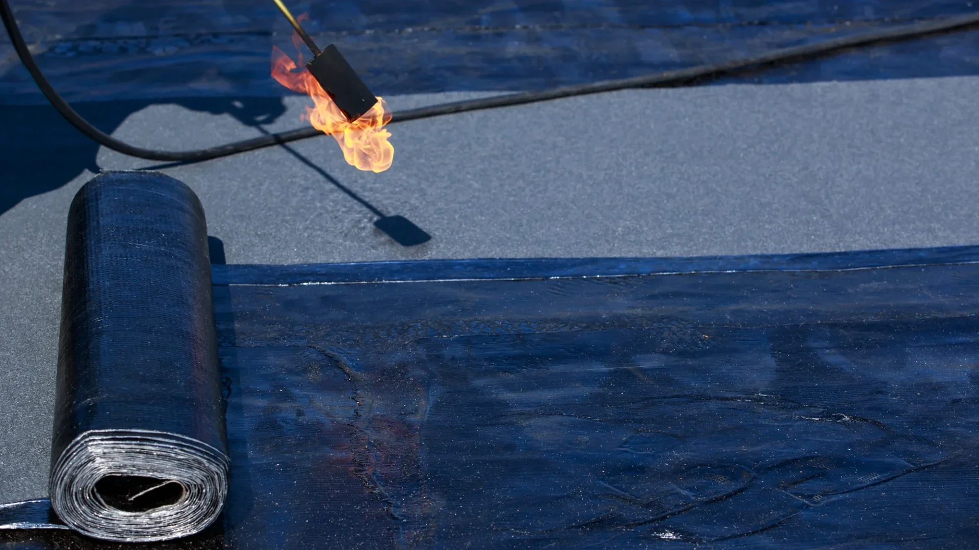 Workers installing new layers of flat rubber roofing with gas torch