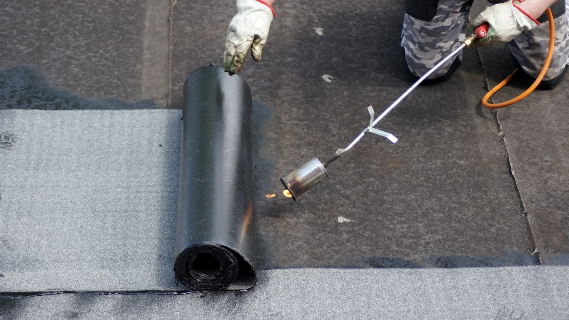 Roofer installing flat rubber roofing with gas torch
