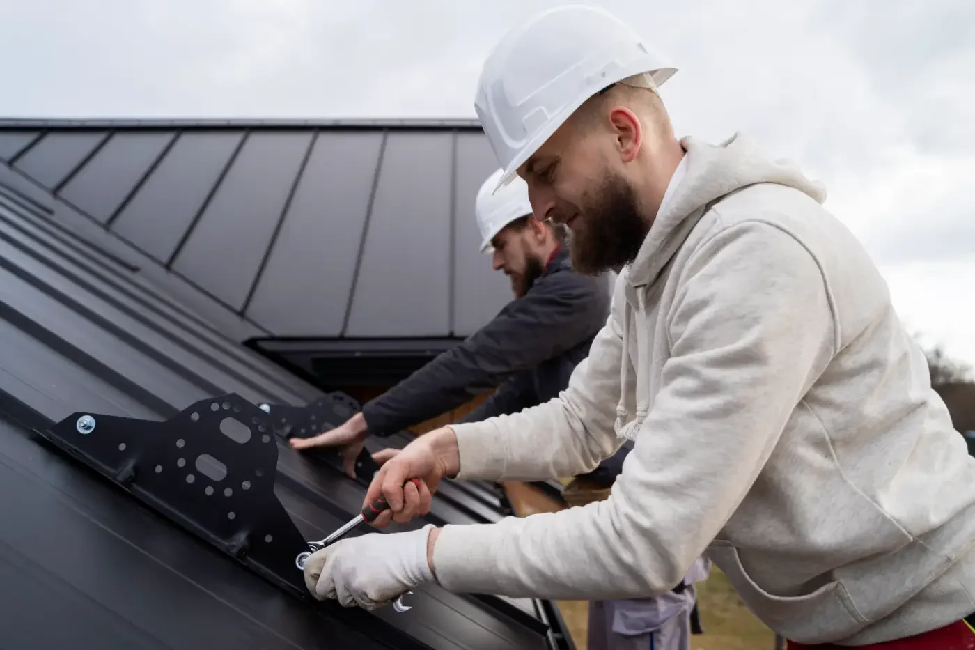 A worker wearing safety gear welds metal components on a building roof during commercial roof repairs.