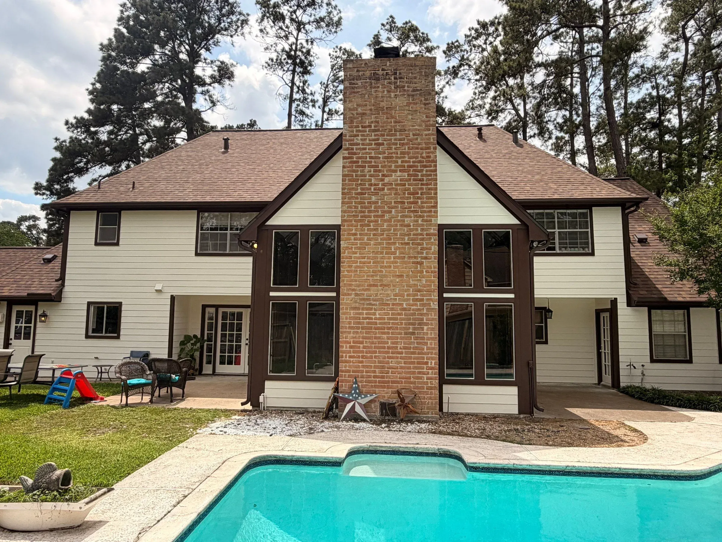 Two-story home with new cream siding and brown trim around a brick chimney, seen from the backyard pool