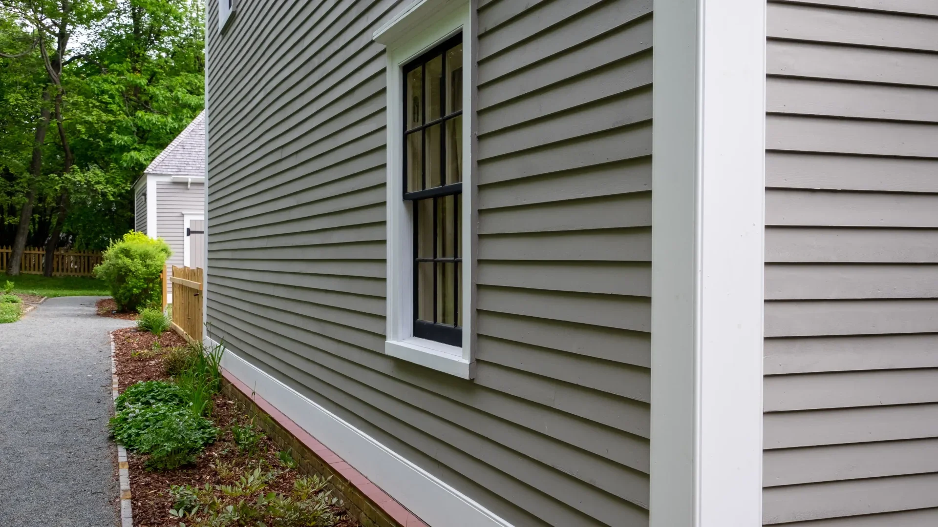 A green two-story house features complex brown shingled rooflines following residential roof repairs.