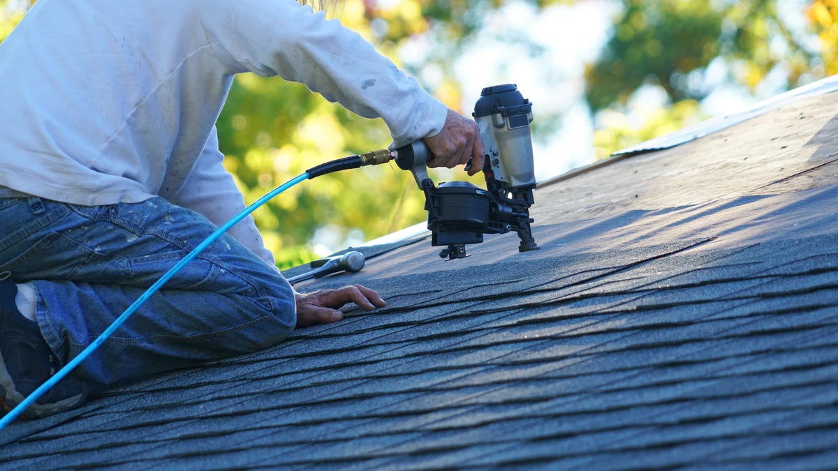 A roofing contractor uses power tools to work on shingled roof edge details during residential roof repairs.